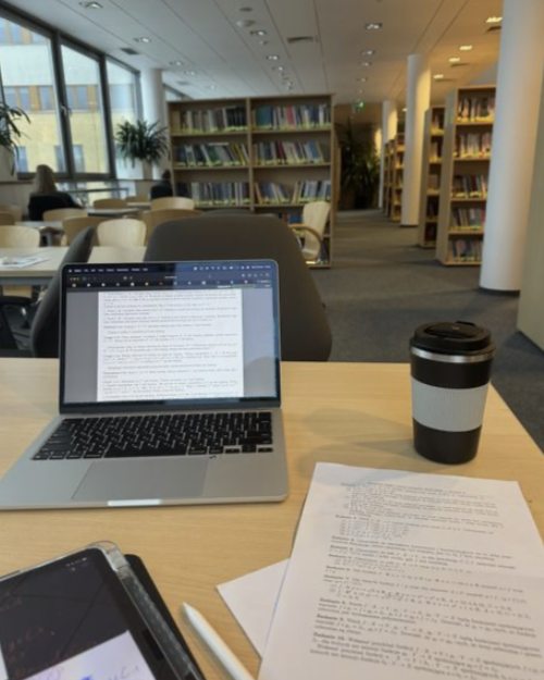 A laptop, notes and coffee on a study desk in a university library